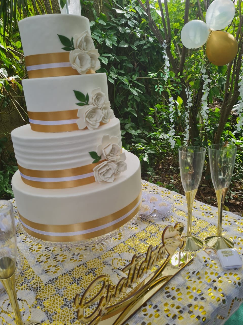 Mesa com bolo branco e dourado em meio à vegetação