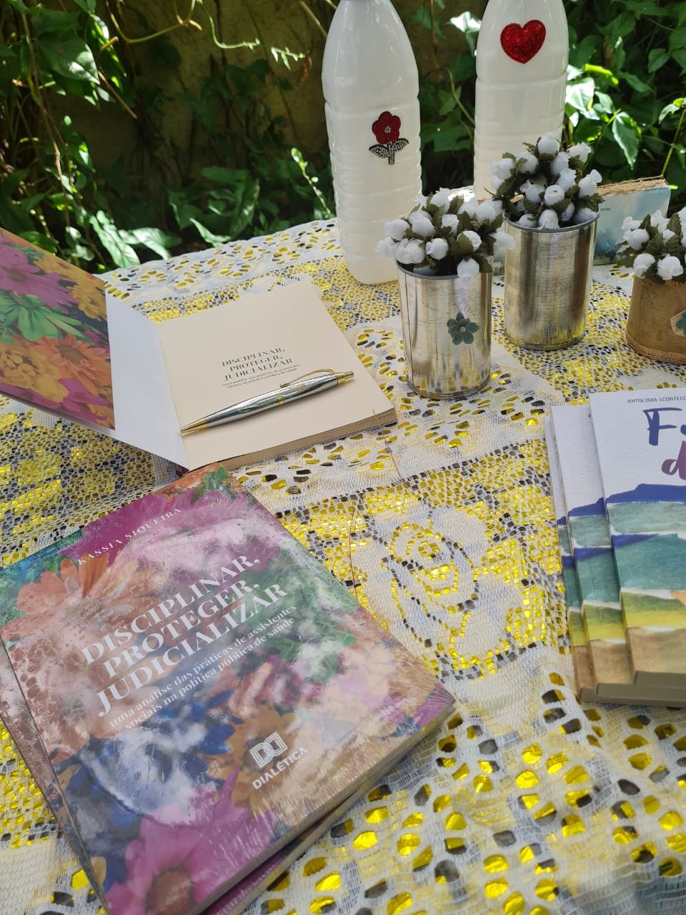 Mesa no jardim com livros, cadernos e arranjos florais artesanais